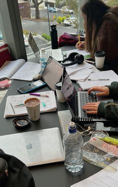 a person sitting at a table with laptops and papers on it, looking out the window