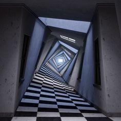 an empty hallway with black and white checkered flooring in the center is lit by two skylights