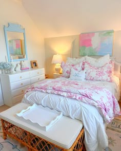 a white bed with pink and green comforter in a bedroom next to a dresser