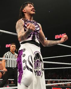 a man with long hair and tattoos standing in a ring next to an official referee