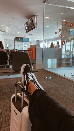 a person sitting on top of a luggage bag in an airport terminal with their feet propped up against the handle