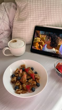 a bowl of fruit and cereal on a table with a tablet next to the bowl