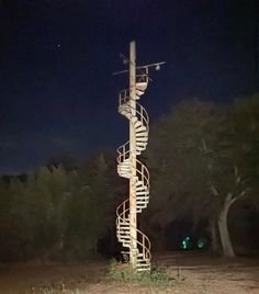 there is a tall spiral staircase in the middle of the field at night with lights shining on it