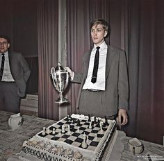 a man standing next to a giant chess board with a trophy in front of him