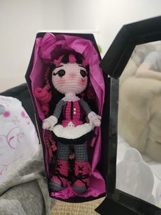 a crocheted doll in a pink and black box on top of a bed