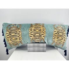 a blue and gold tiger pillow with tassels on the edges, sitting on a white table