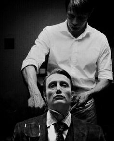 a man is getting his hair cut by another man in a suit and tie, while holding a glass of wine