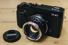 a camera sitting on top of a wooden table next to a small lens cap with the word pentax printed on it