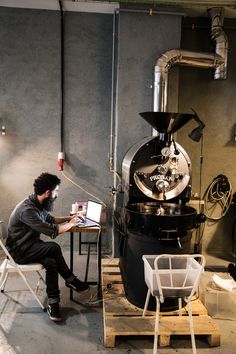 a man sitting at a desk in front of a coffee machine working on a laptop