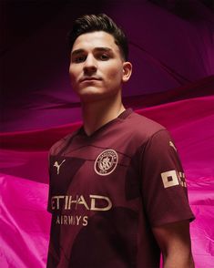 a young man in a soccer uniform poses for a photo against a pink background with an umbrella