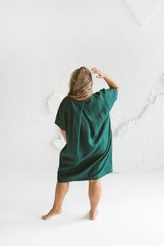 a woman standing in front of a white wall wearing a green dress and holding her hands behind her head