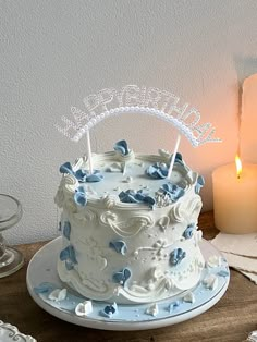 a white cake with blue butterflies on it sitting on a table next to two candles