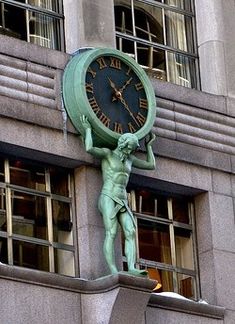 a clock on the side of a building with a statue holding it's head