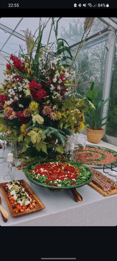 a table topped with plates filled with food next to a vase full of flowers and greenery