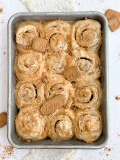 a pan filled with cinnamon rolls on top of a white countertop next to cookies