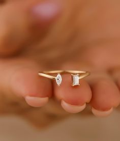 a close up of a person's hand holding a gold ring with two stones