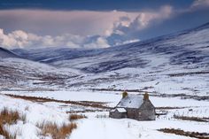 a small house in the middle of a snowy field with mountains in the back ground