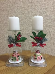 two glass vases with christmas decorations on top of a table next to a candle