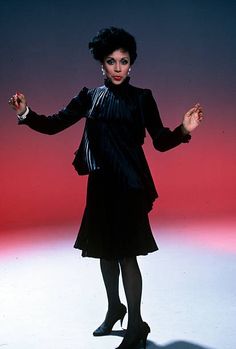 a woman in a black dress is standing with her arms out and hands extended up