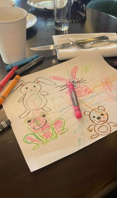 a child's drawing on paper with crayons next to it and two pens