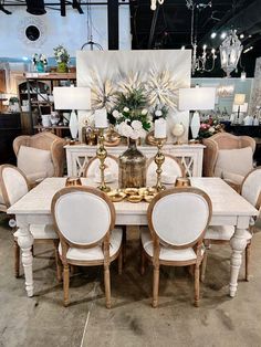 a dining room table with chairs and chandelier in front of a large painting