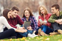 four young people are sitting on the grass and looking at something in their lap top