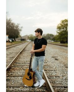 a man standing on train tracks holding a guitar