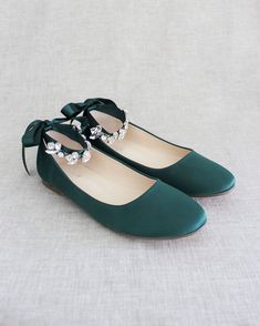 a pair of green shoes with bows on the side and pearls in the middle, sitting on a white surface