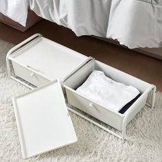 two white boxes with shirts in them sitting on the floor next to a bed and pillows