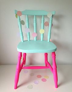 a pink and blue wooden chair with polka dots on the floor in front of a white wall