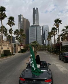 a woman sitting in the back of a convertible car with a green scarf on top