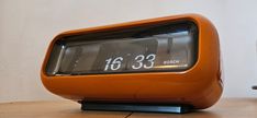 an orange clock sitting on top of a wooden table