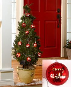 a small christmas tree with ornaments on it in front of a red door and an ornament that says merry christmas