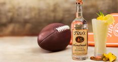 a bottle of titos vodka next to a football and a glass with a drink in it