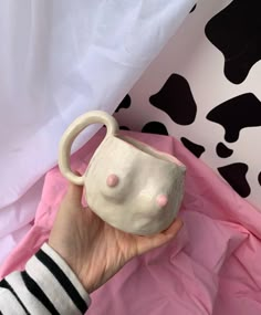 a hand holding a white ceramic cup with pink polka dots on the outside and black spots on the inside