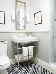 a white toilet sitting next to a sink in a bathroom under two framed pictures on the wall