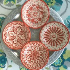 four red and white plates sitting on top of a floral tablecloth covered table cloth