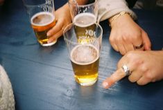 several people are sitting at a table with beers in their hands and pointing to the side