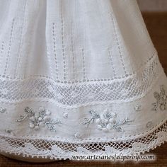 a white dress with lace and flowers on the bottom is sitting on a wooden floor