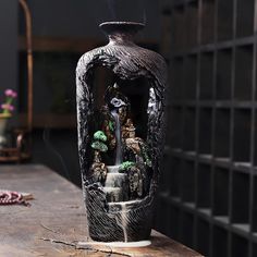 a black vase sitting on top of a wooden table next to a potted plant