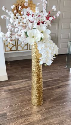 a gold vase filled with white flowers on top of a wooden floor