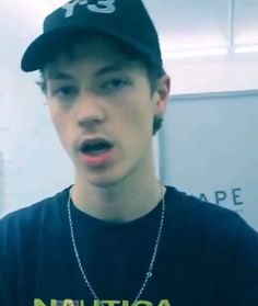 a young man in a black shirt and hat making a surprised face with his mouth open