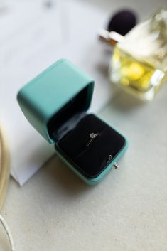 an open ring box sitting on top of a table next to a bottle of perfume