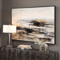 a large painting hangs on the wall next to a table with a lamp and books