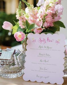 pink flowers are in a vase next to a menu card on a table with other items