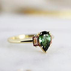 Pear Green Tourmaline Engagement Ring, Three Stone Ring, 14k Solid Gold Tourmaline Engagement Ring, Dark Green Gemstone Ring, Gift For Her DETAILS ABOUT THE RING, MATERIAL AND STONES *** Band is 14k yellow gold and 1.3mm *** Stone is pear cut dark green tourmaline 8x5mm ***Baguette pink tourmalines are 4mm x 2mm each side *** Ready to ship US Size 7 If you need another size please leave me a message, It could be resized in a week. If you have any questions regarding this item, please hit the “As Dark Green Gemstone, Green Tourmaline Engagement Ring, Engagement Ring Three Stone, Tourmaline Engagement Ring, Ring Three Stone, Green Gemstone Ring, Three Stone Ring, Green Gemstones, Three Stone Rings