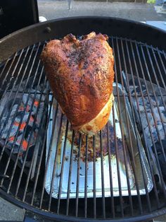 a large piece of meat is cooking on a bbq grill with other food items