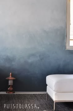 a white couch sitting next to a window on top of a carpeted floor in front of a blue wall