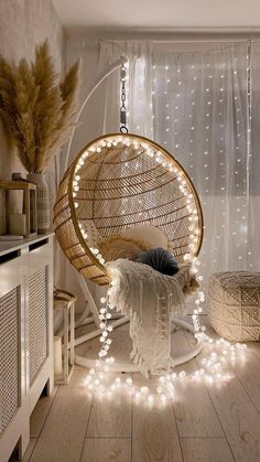 a hanging chair with lights around it in a room that has white curtains and wooden floors