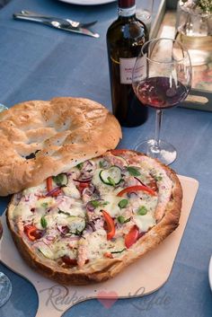 a pizza sitting on top of a wooden cutting board next to a bottle of wine